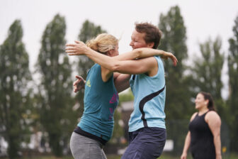 Two women stand on a sport field. They are wearing sports gear and embracing in celebration.