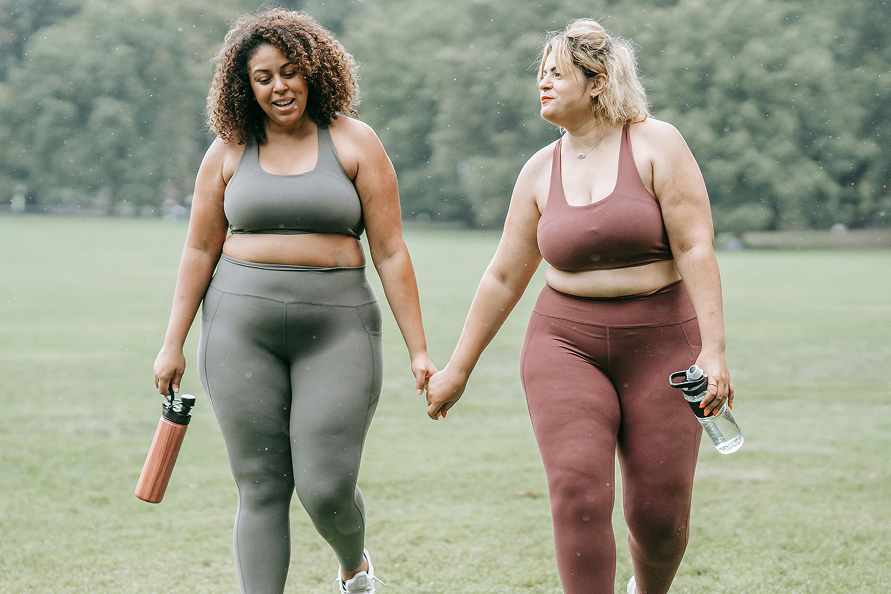 Two women in sports wear hold hands as they walk across a field.
