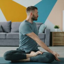 A man sits in the lotus position in a living room.