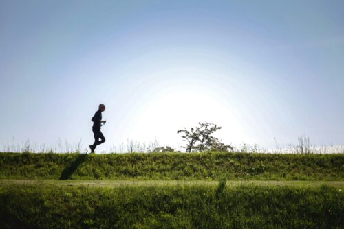A man runs along an embankment in the sunshine.